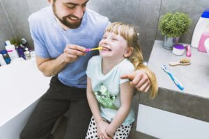 cheerful father helping daughter brush teeth 300x200 1